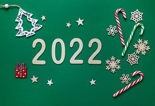 New Year's composition on a green background with wooden numbers 2022, snowflakes, sweet caramel, Christmas toy Christmas tree. Flat lay, top view, christmas card