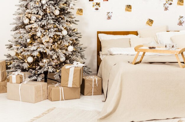 New Years bright interior bedroom with decorated Christmas tree with garlands white bed beige blanket photos on the wall Christmas interior Scandinavian style Location for photo shoot