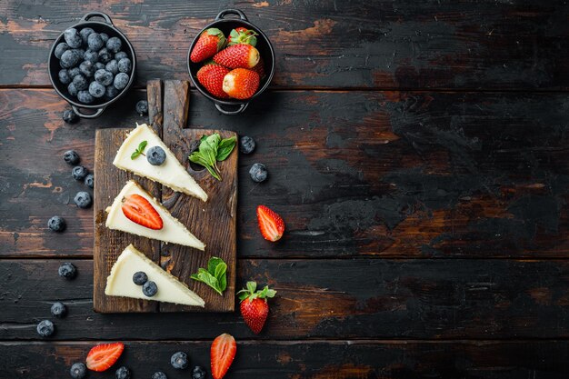 New York cheesecake or classic cheesecake with fresh berries, on old dark  wooden table background, top view flat lay with copy space for text