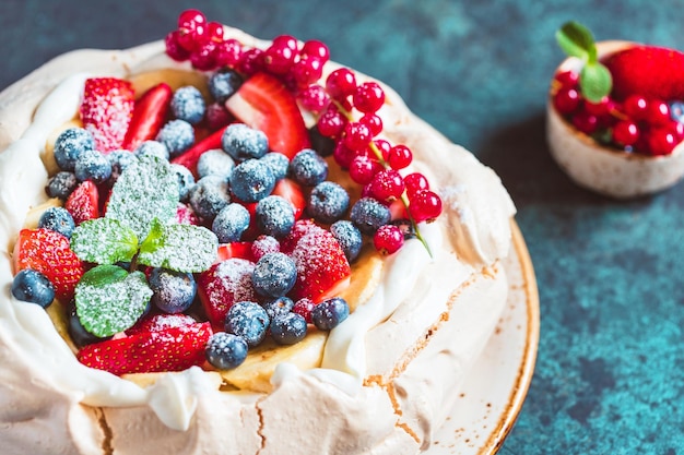 New Zealand Pavlova cake with whipped cream and mix of fresh berries on a blue textured background