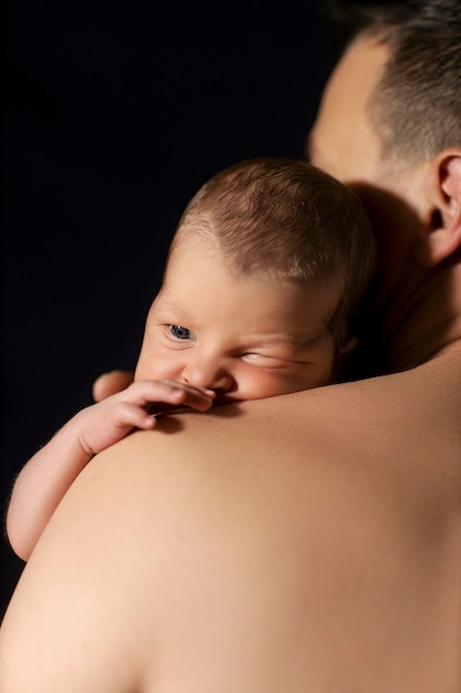 newborn baby in the arms of dad on a black background