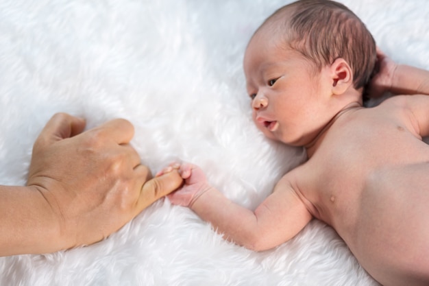 Newborn baby boy holding little finger of father's hand