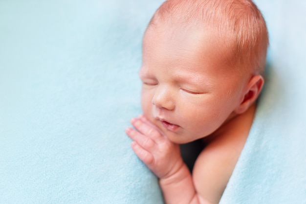 Newborn baby boy sleeping on the blue close-up