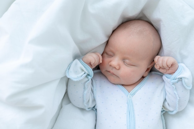 Newborn baby boy sleeps seven days in a cot at home on a cotton bed closeup