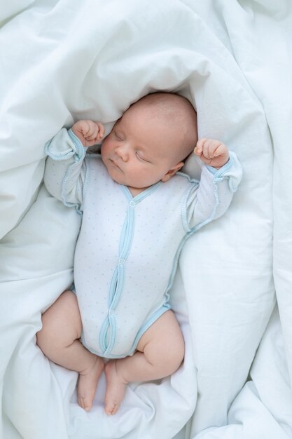 Newborn baby boy sleeps seven days in a cot at home on a cotton bed, top view.