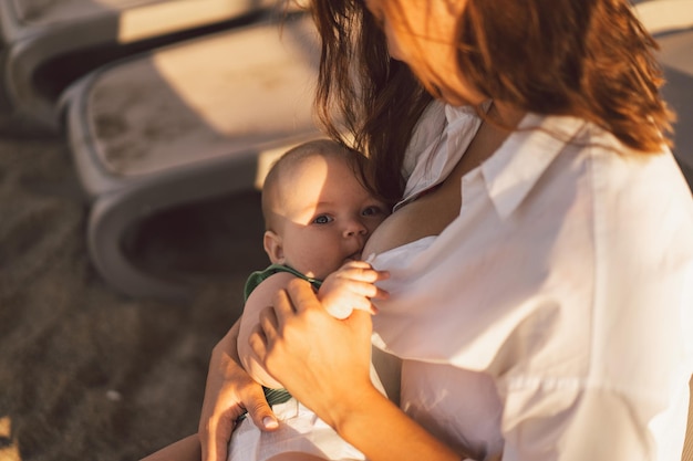 Newborn baby boy sucking milk from mothers breast on the beach