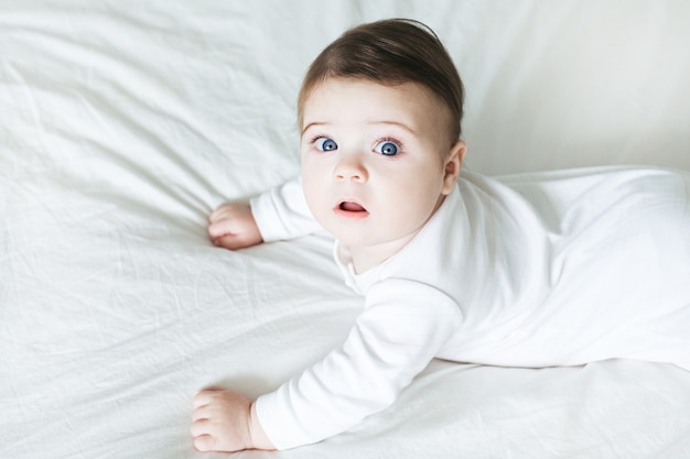 Newborn baby boy in white clothes on bed at home top view