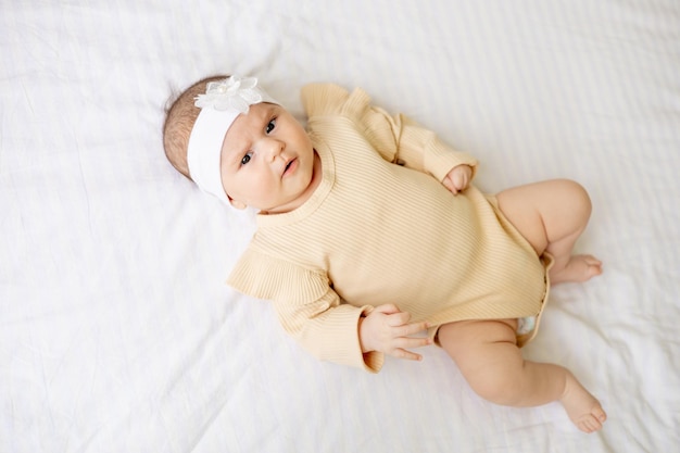 a newborn baby in a crib in a brown warm jumpsuit on a white cotton bed has woken up in the morning or is falling asleep a surprised portrait of a baby