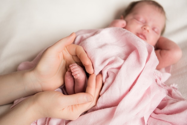 Newborn baby feet in mother hands on pink fabric