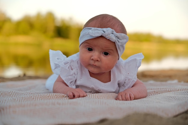 Newborn baby girl lies on the beach in a white dress