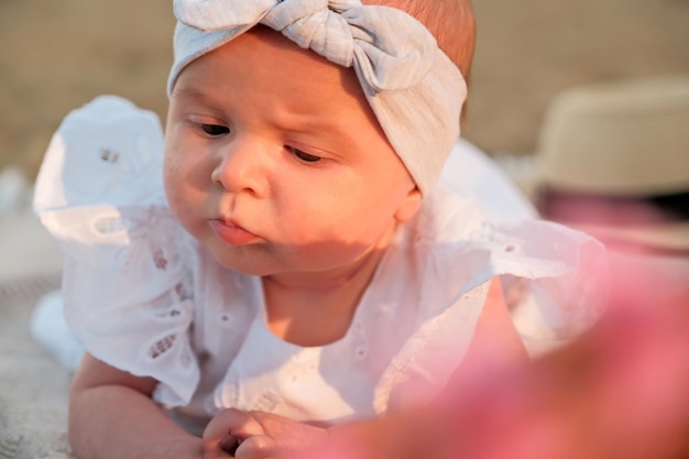 Newborn baby girl lies on the beach in a white dress