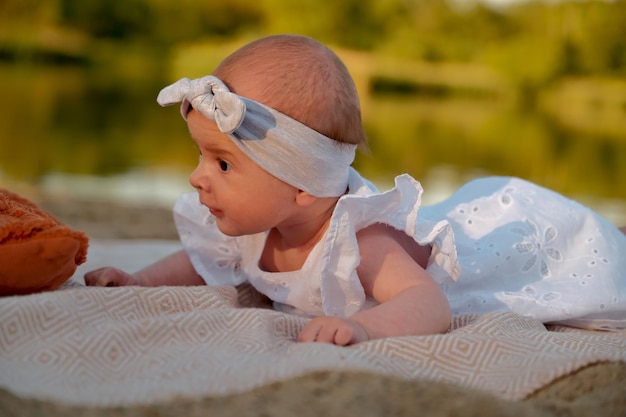 Newborn baby girl lies on the beach in a white dress