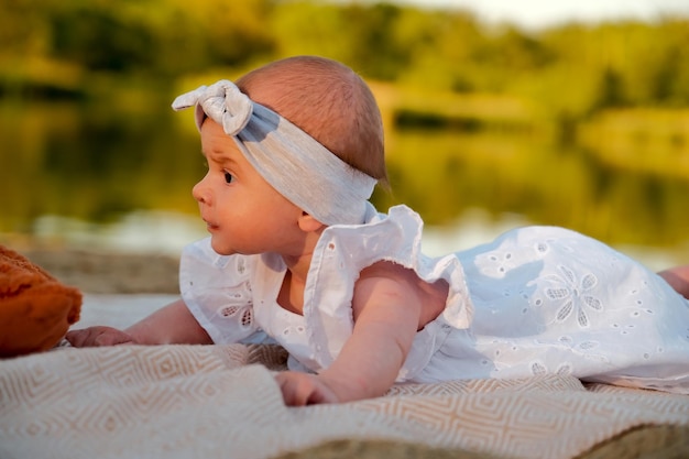 Newborn baby girl lies on the beach in a white dress