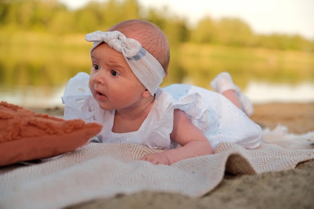 Newborn baby girl lies on the beach in a white dress