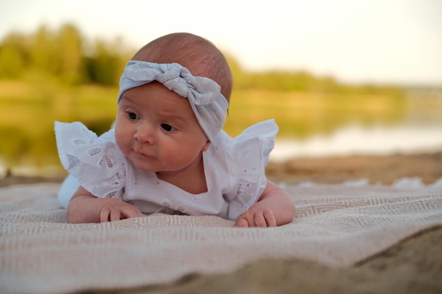 Newborn baby girl lies on the beach in a white dress