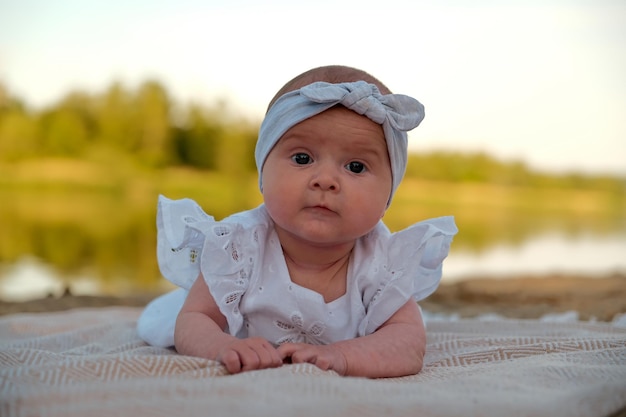 Newborn baby girl lies on the beach in a white dress