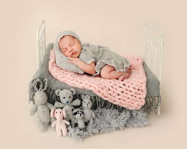 Newborn baby girl sleeping in tiny bed decorated with knitted toys. Adorable infant child kid napping during studio photoshoot