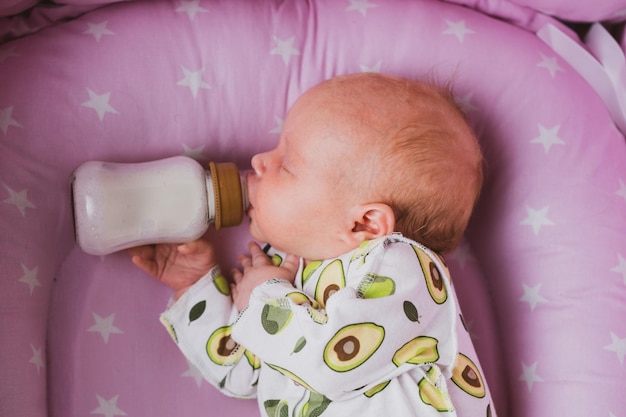 A newborn baby independently drinks milk or a formula milk from a bottle at home