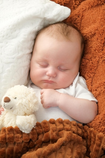 A newborn baby sleeps on a bed A teddy bear lies nearby mother and child