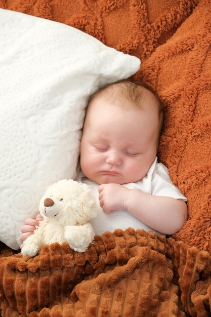 A newborn baby sleeps on a bed A teddy bear lies nearby mother and child