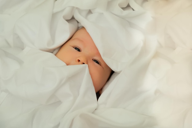 Newborn baby smiles and laughs shows emotions baby lies on a white cloth