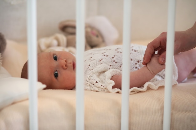 Newborn cute baby lies in the crib and looking at mother