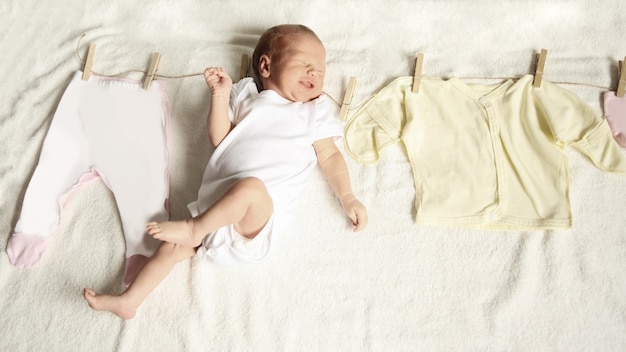 Newborn infant and baby clothes on a wooden primako on a light b