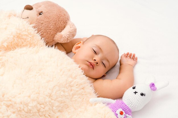 A newborn sleeps with his favorite toys under a blanket.