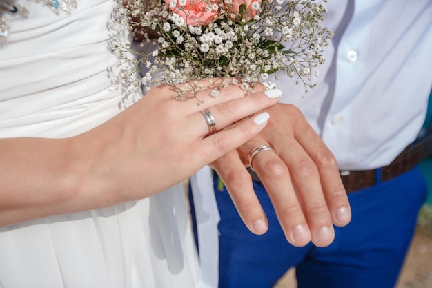 Newlywed couple holding hands and displaying wedding rings wedding bouquet on altar in church Hands and rings on wedding bouquet