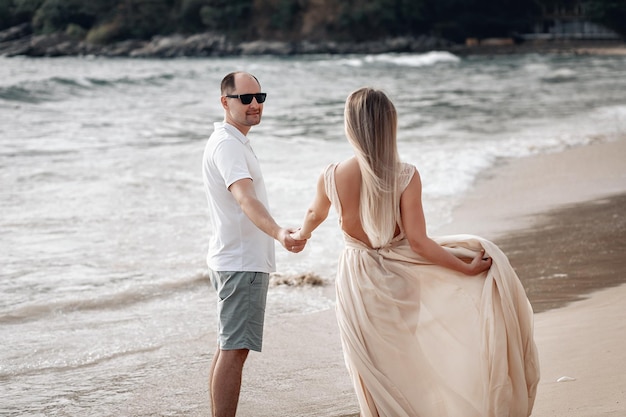 Newlyweds dressed in white holding hands on an exotic beach  sea, sand and love; honeymoon concept.