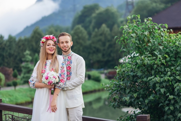 Newlyweds in embroidered clothes smiling and looking at the camera against the background of mountains and lakes.