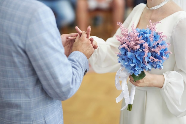 the newlyweds exchange rings, the bride holds a bouquet of blue hydrangeas and dried flowers in hand