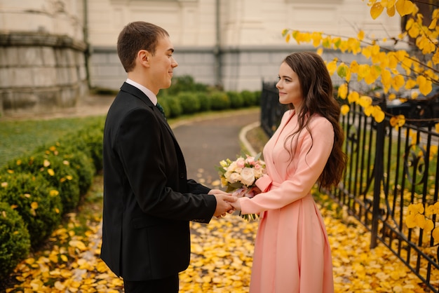 Newlyweds groom and bride walking in autumn park near vintage atmosphere gothic cathedral.