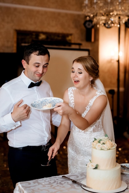 Newlyweds happily cut, laugh and taste the wedding cake