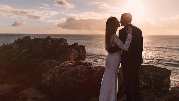 Newlyweds hugging and kissing on the rocky shore of the ocean ov