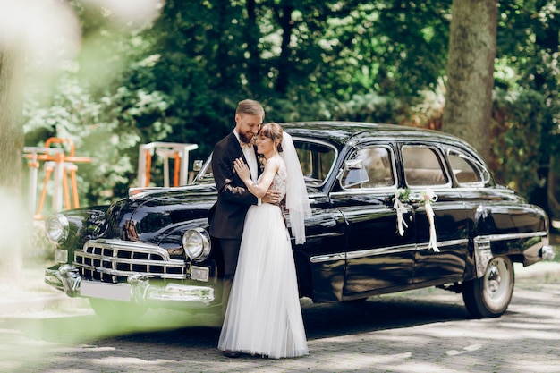 Newlyweds kiss behind an old American car