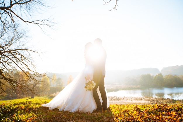 Newlyweds kissing and smiling on their wedding day on the walk outdoors. Funny bride with bouquet of flowers.