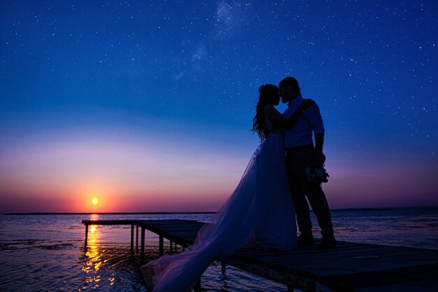 Newlyweds on the ocean at sunset. a couple in love only that celebrated the wedding in wedding dresses stand on a wooden bridge in the sea against the backdrop of a beautiful sunset.