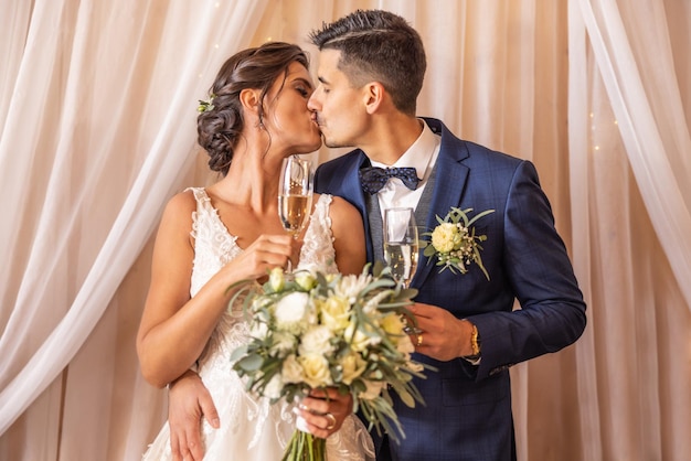 Newlyweds that just got married are having their first kiss with champagne in their hands