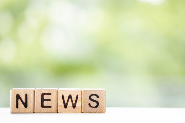 NEWS word is written on wooden cubes on a green summer background Closeup of wooden elements