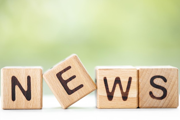 NEWS word is written on wooden cubes on a green summer background Closeup of wooden elements