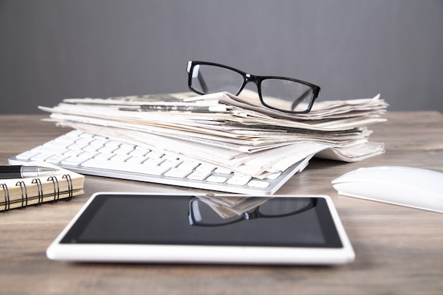 Newspapers, computer keyboard, eyeglasses on the wooden table.