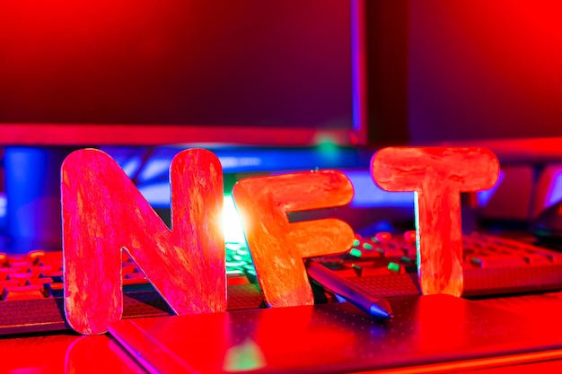 NFT Non-Fungible Token text of letters illuminated with neon light. Workplace of a graphic designer creating NFT digital art. Concept of cryptoart and blockchain technology