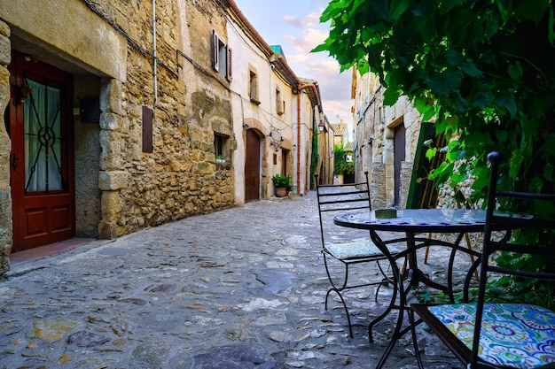 Nice alley full of stone houses and iron table and chairs to rest Peratallada Girona Spain