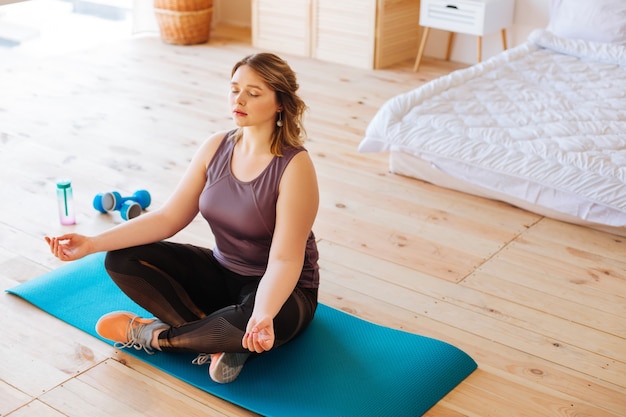 Nice attractive woman feeling relaxed while practicing yoga at home