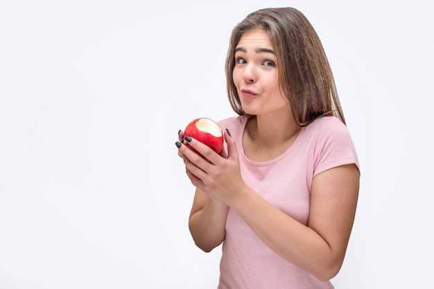 Nice and attractive young woman looks at the camera and hold bitten apple