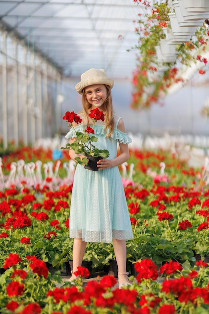 Nice child girl in a turquoise dress in the greenhouse and looking at camera