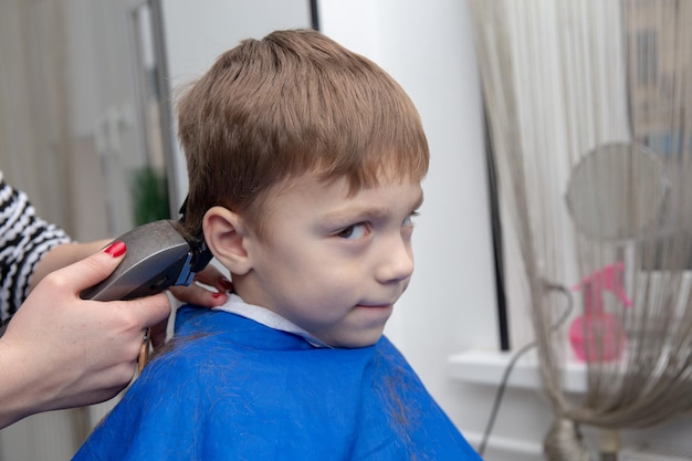 Nice european little boy getting hairstyle in barbershop