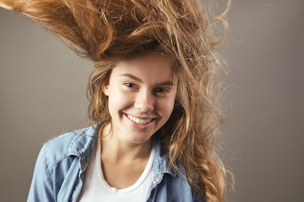 Nice girl with long brown flowing hair smiles on a gray background .