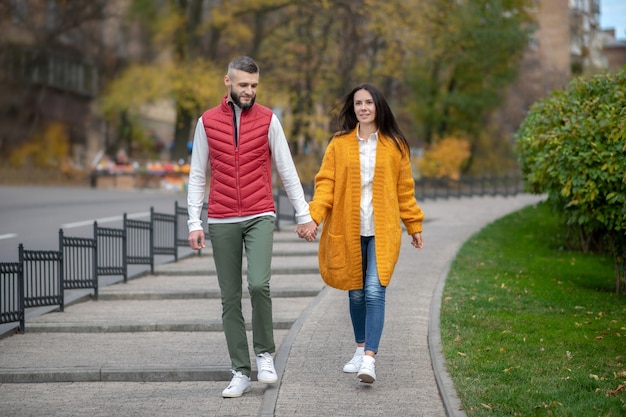 Nice happy couple holding their hands together while walking along the street